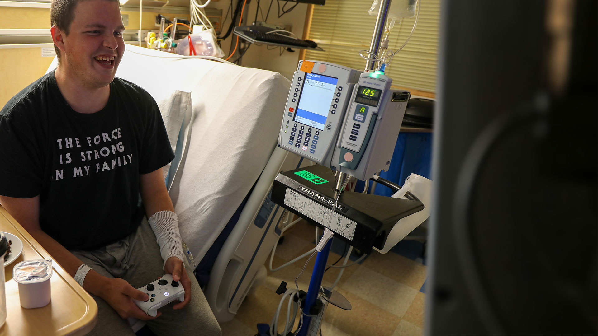 A young patient laughing while playing Xbox from his hospital bed